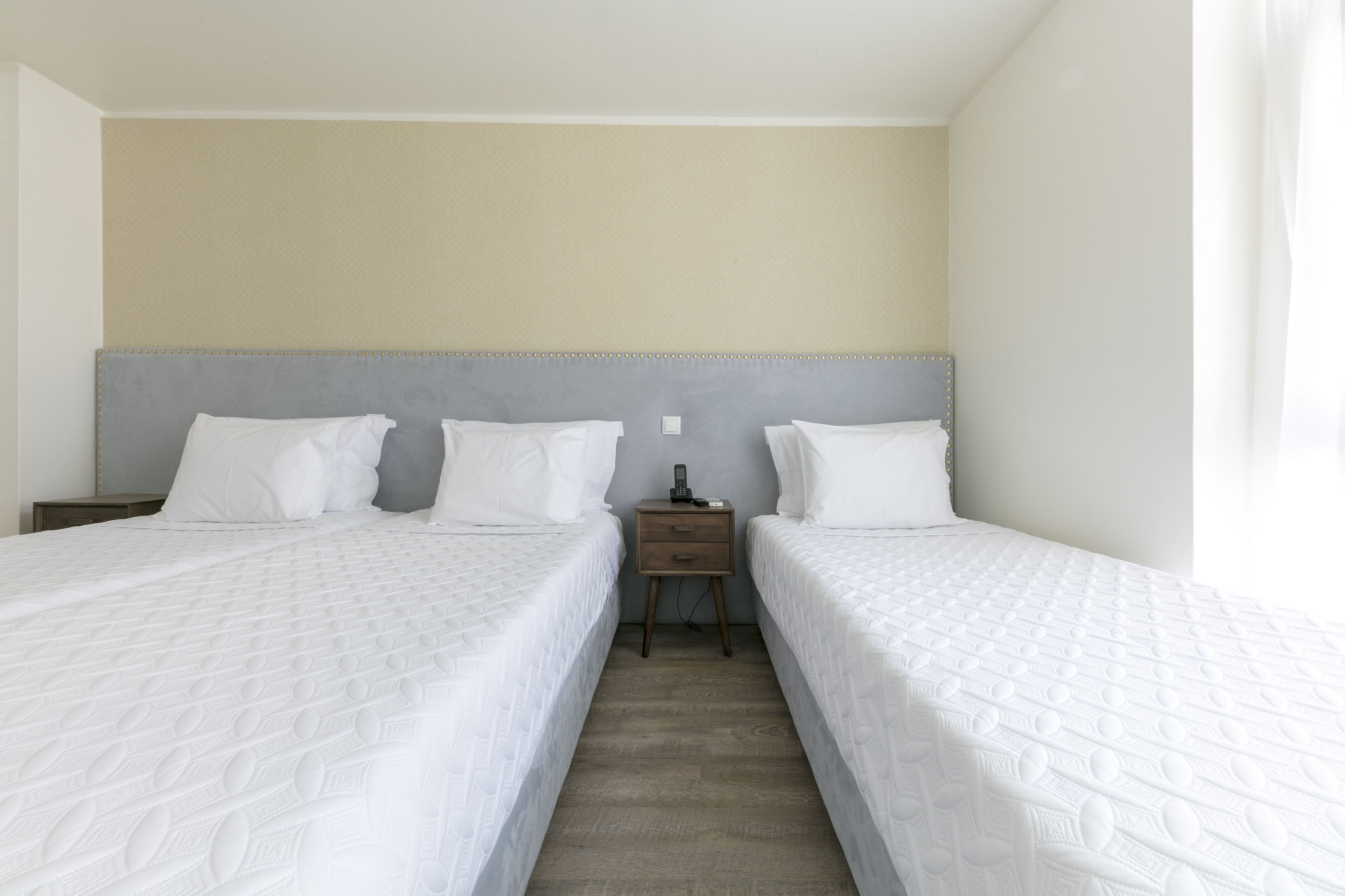 Habitación de hotel con dos camas individuales, una mesita de noche entre ellas y una pared lisa arriba.