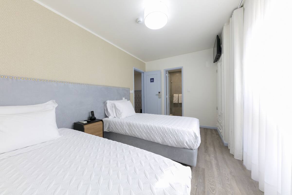 A hotel room with two beds, a nightstand, a TV, and a door leading to another room.