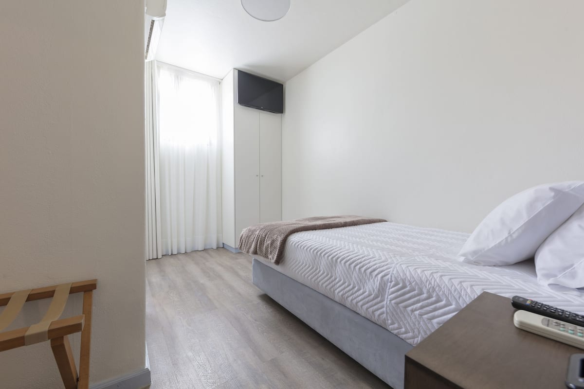A bedroom with a bed, a TV mounted on the wall, and a wooden nightstand with a remote control.