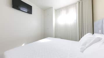A hotel room with a bed, a flat-screen TV mounted on the wall, and a window with curtains.