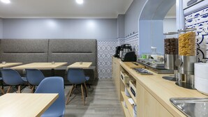 A modern cafe with grey cushioned seating, blue chairs, and a breakfast bar with various food items. - D' El Rei B&B (Matosinhos)