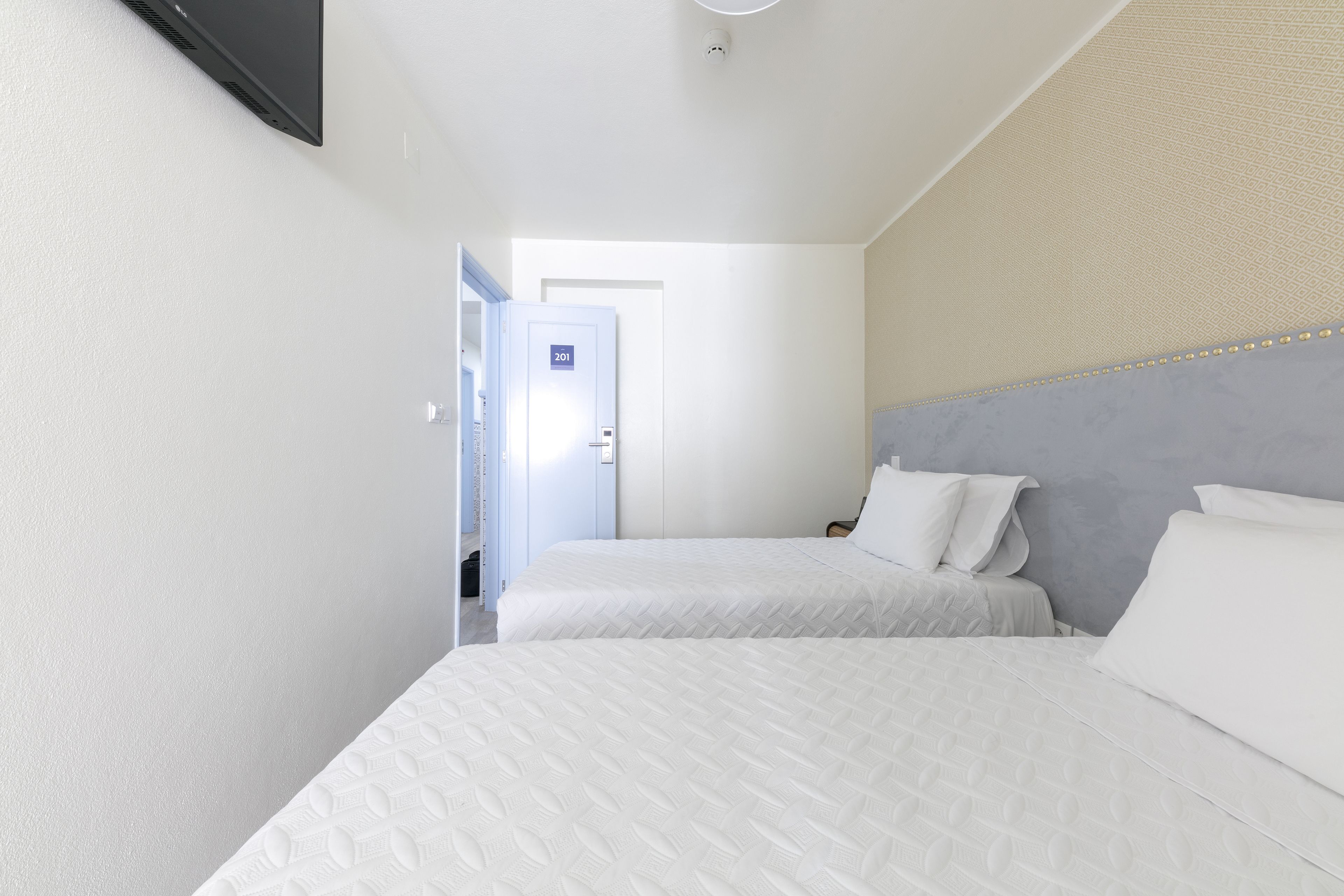 Habitación de hotel con dos camas, un televisor de pantalla plana montado en la pared y una puerta con un letrero con número.