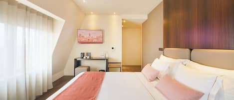 A modern hotel room with a large bed, a desk, and a cityscape view.