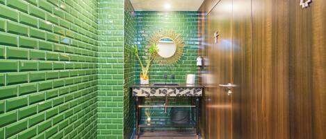 A bathroom with green tiled walls, a wooden door, and a mirror above the sink.