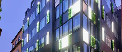 A modern building with multiple floors, large windows, and green plants on the exterior.