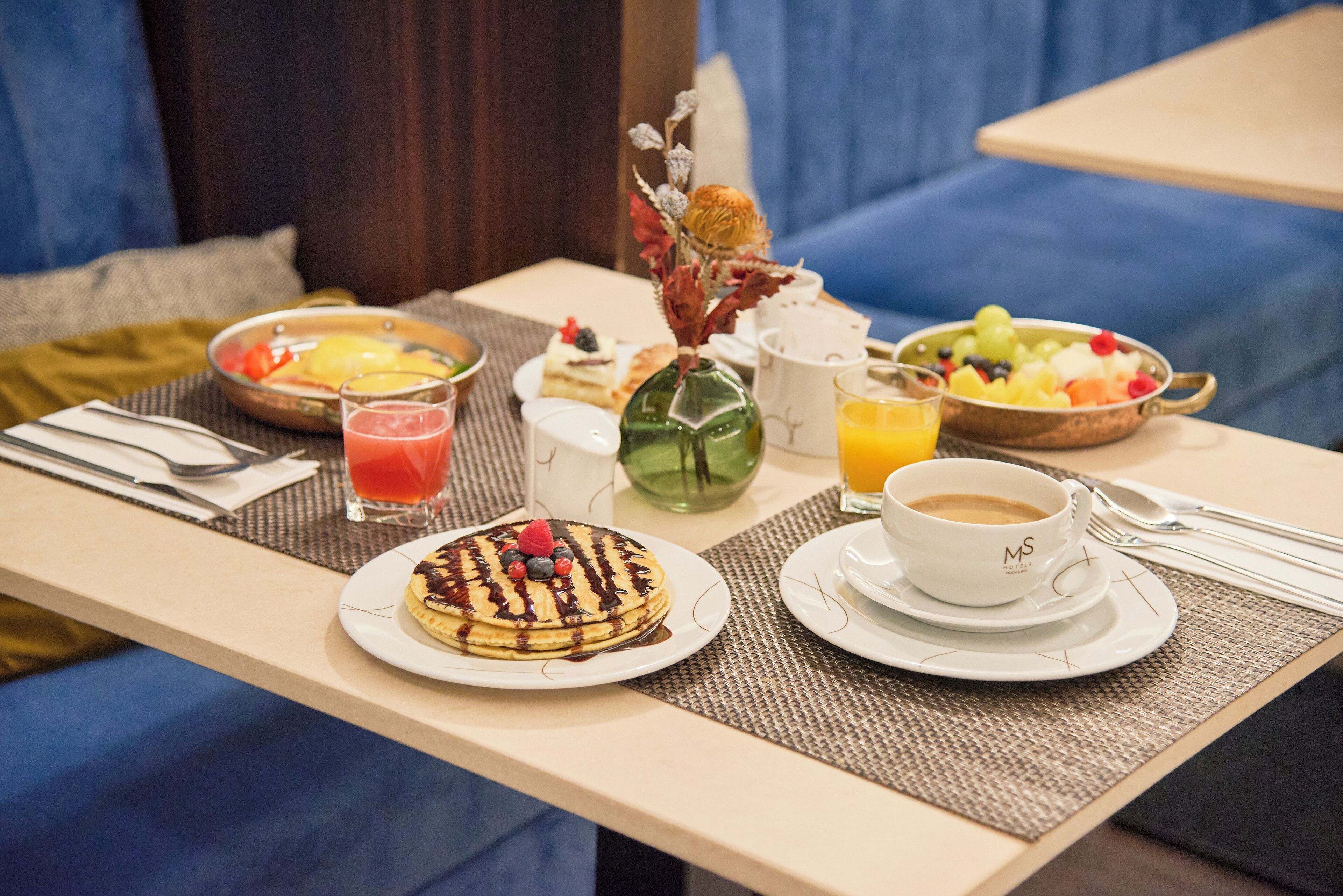 A breakfast table with pancakes, fruit, coffee, and juice.