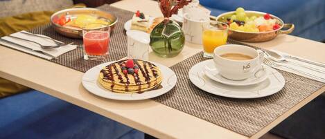 A breakfast table with pancakes, fruit, coffee, and juice.