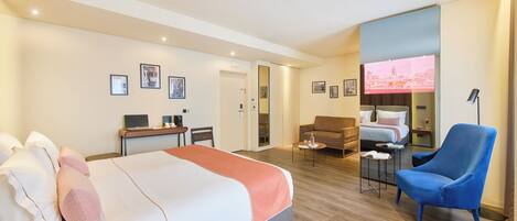 A hotel room with a large bed, a desk, a chair, a TV, and a sofa.