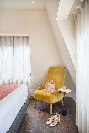 Relax in a stylish room with a large bed, a comfortable armchair, and a window with sheer curtains.