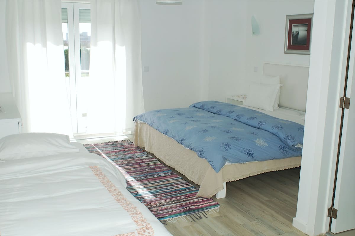 A bedroom with a bed, a bedside table, a nightstand, a window with curtains, and a door.