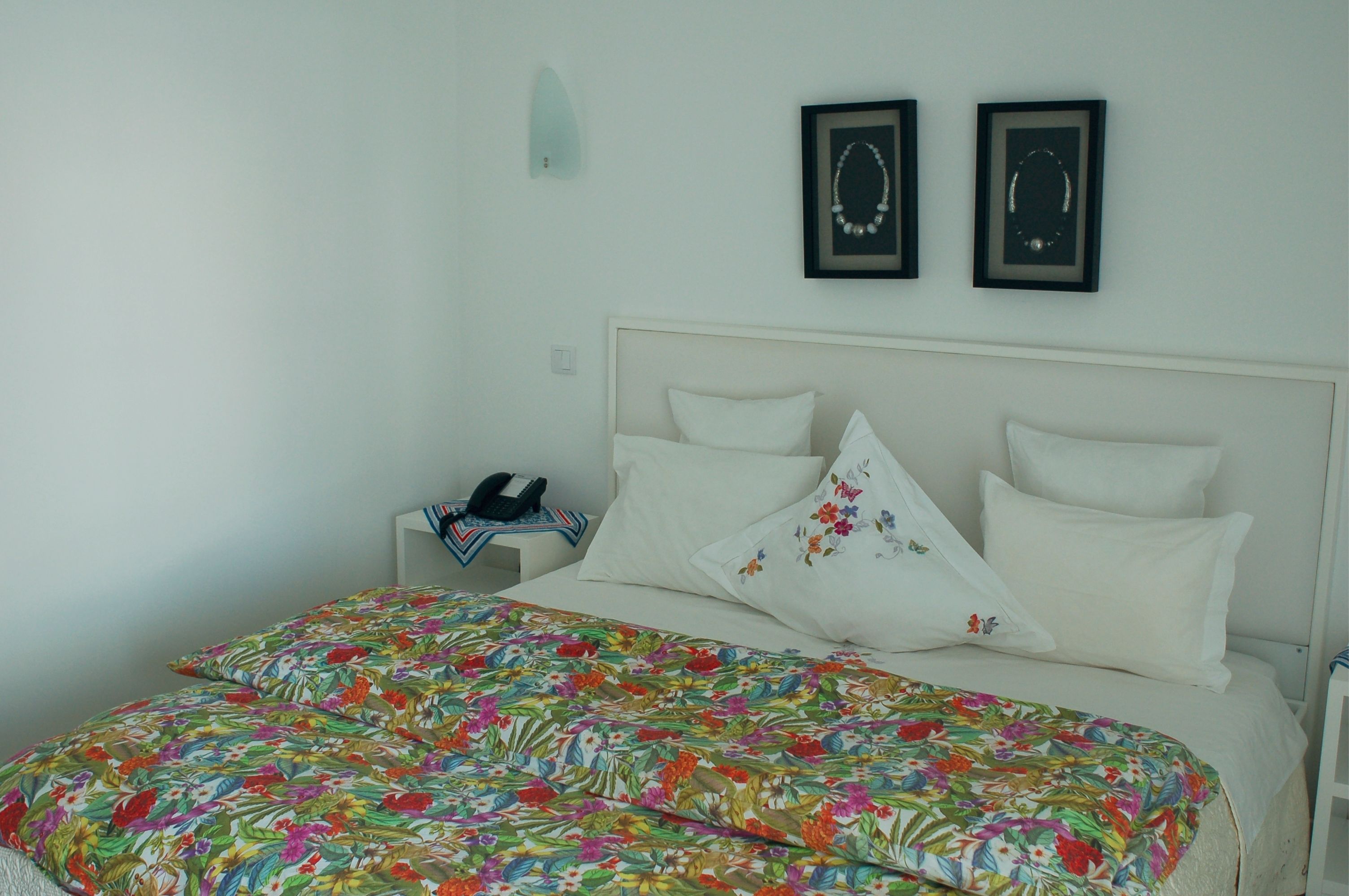 A bedroom with a bed, white walls, a nightstand, and two framed pictures.