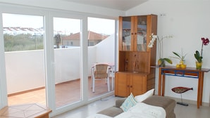 A living room with a sofa, a wooden cabinet, a small table, and a view through a sliding glass door to an outdoor balcony. - Hotel Baleal Spot (Peniche)