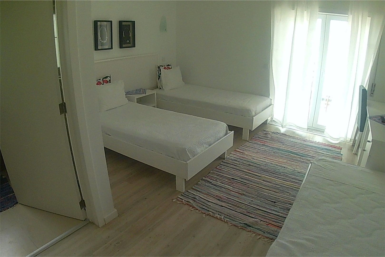 A bedroom with two single beds, a bedside table, a small chair, and a window with curtains.