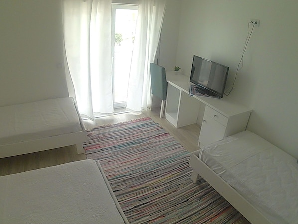 Un dormitorio con dos camas, un escritorio, un televisor y una ventana con cortinas.