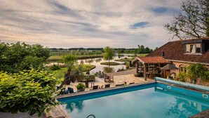 A swimming pool with a view of a river and a wooden deck with outdoor furniture. - Guesthouse Ensenada (Schoondijke)