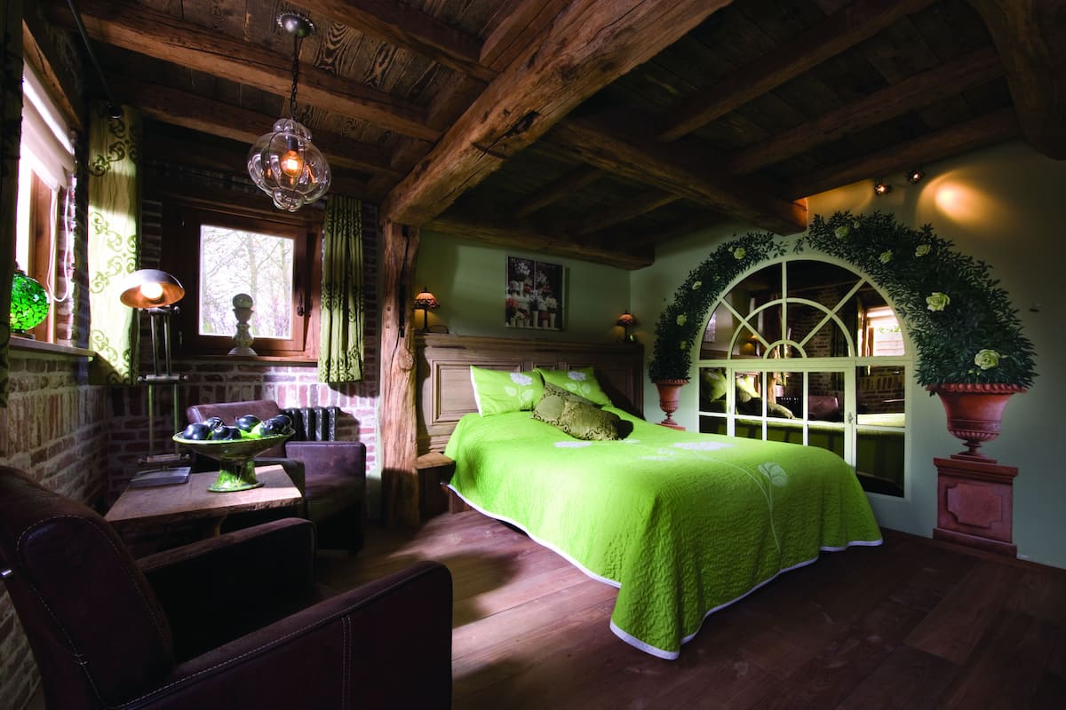 Um quarto acolhedor com teto de madeira, cama verde, mesa de jantar com cadeiras e janela com cortinas.