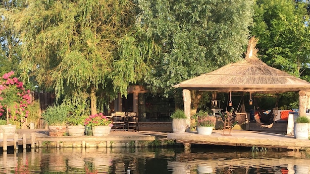 A tranquil garden with a gazebo, a wooden dock, and a pond reflecting the surroundings. - Guesthouse Ensenada (Schoondijke)