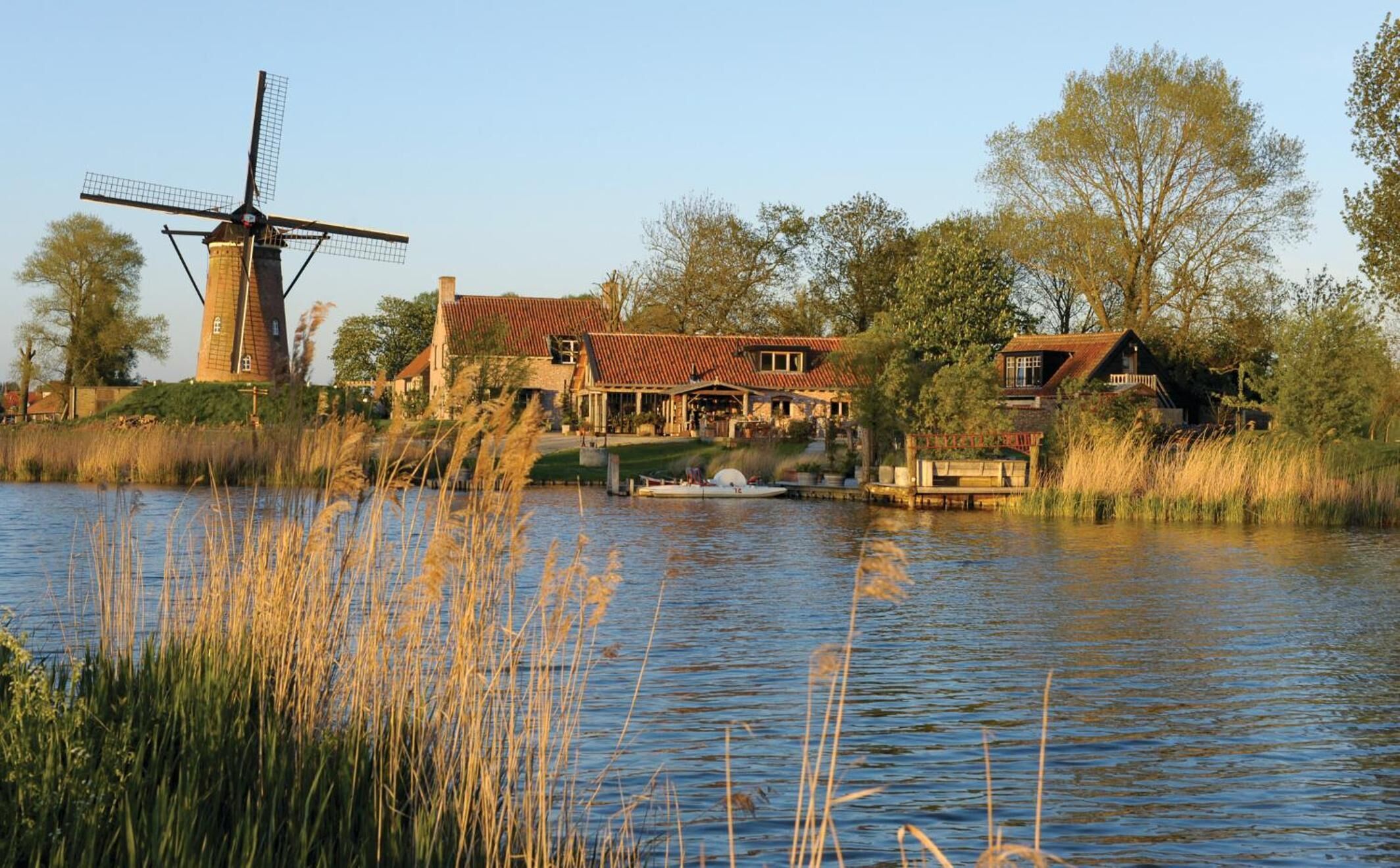 A traditional windmill, a riverside house with a red roof, and a dock with a boat.