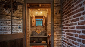 A rustic bathroom with exposed brick walls, a stone sink, and a window with wooden shutters. - Guesthouse Ensenada (Schoondijke)