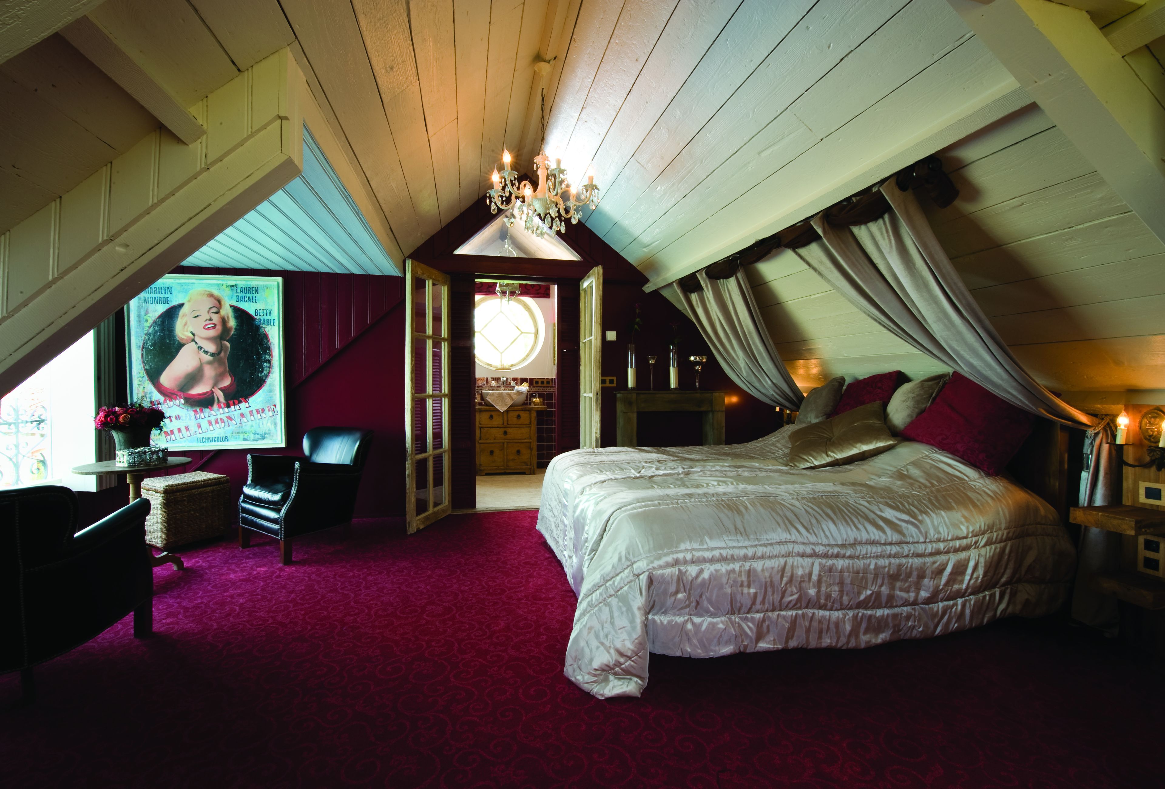 A bedroom with a large bed, a chandelier, a desk with a chair, and a poster on the wall.