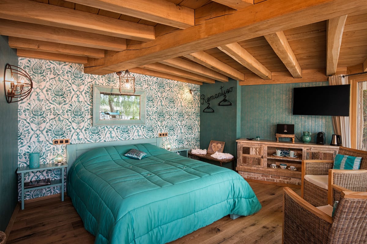 Quarto com cama grande, vigas de madeira no teto, televisão e lareira de tijolos.