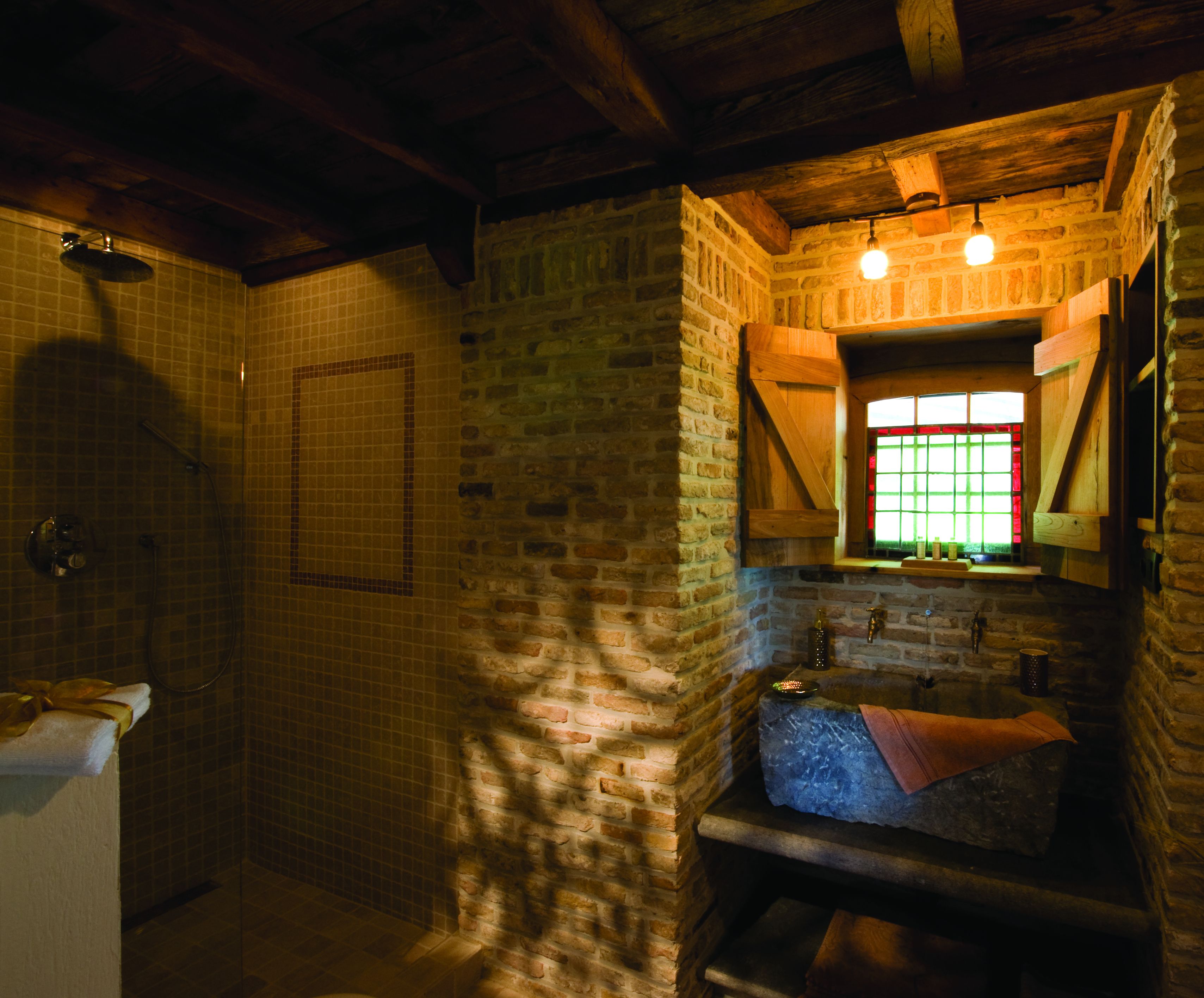 A rustic bathroom with a shower, a sink, and a window with a stained glass design.