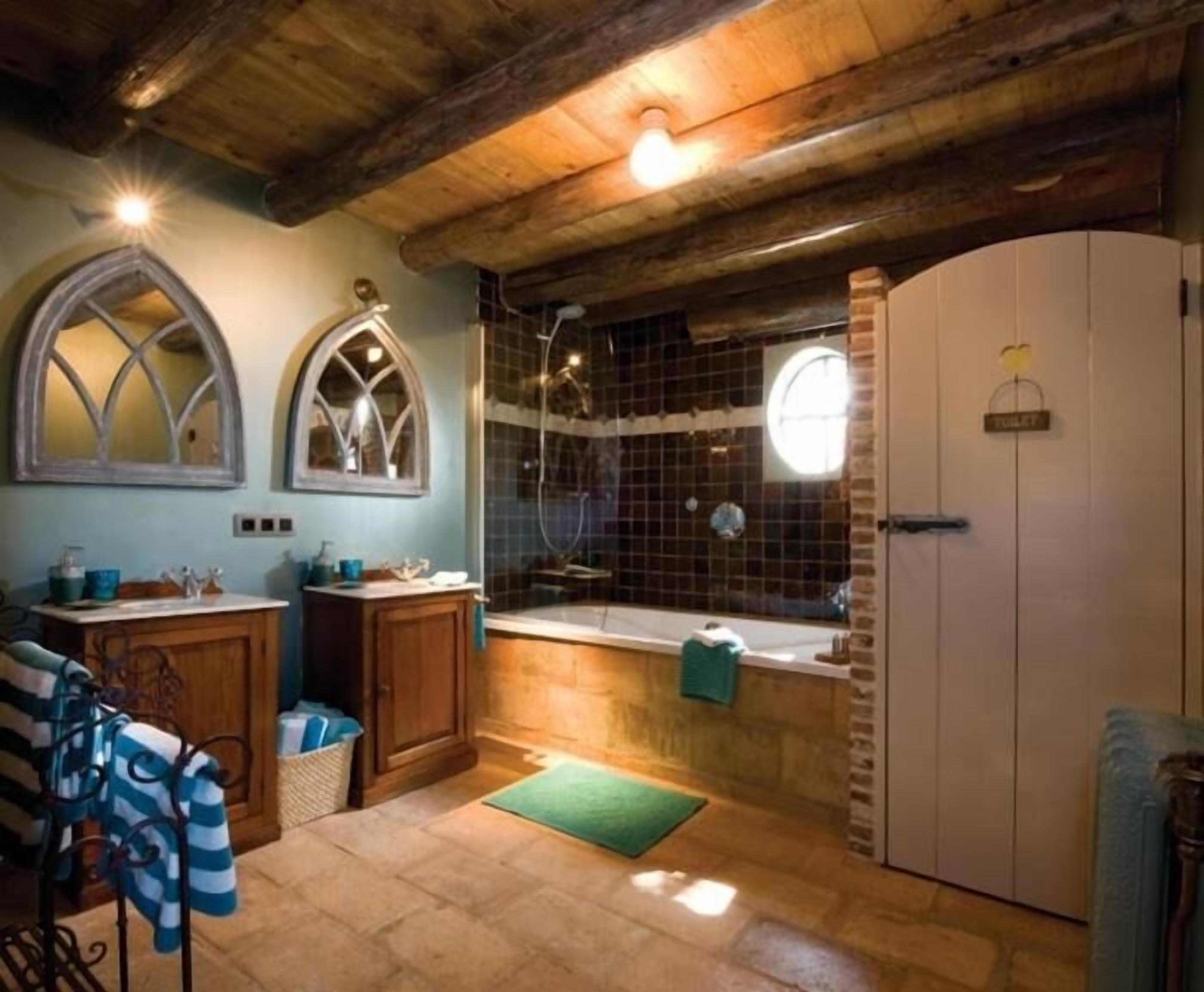 A rustic bathroom with a wooden ceiling, a bathtub, a shower, and a toilet.