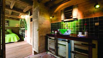 Een rustiek houten interieur met een groene tegeltjeswand, houten balken en een bed met een groene dekbedovertrek.