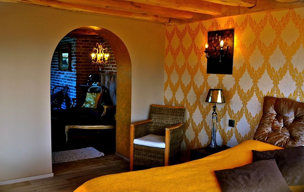 A cozy room with a bed, a chair, a lamp, and a patterned wall.