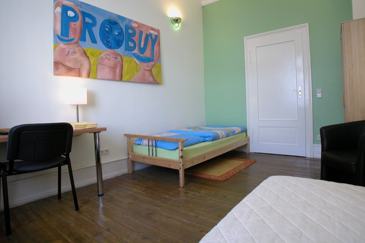 Una habitación con cama, escritorio, silla y un cuadro en la pared.