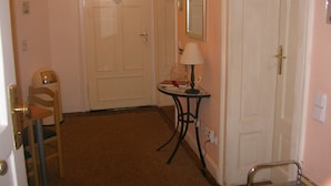 A hallway with a door labeled "Bathroom Bad," a chair, a small table with a lamp, and a metal chair. - CoLodging (Mannheim)