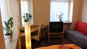 A hotel room with a bed, a desk, a chair, a television, and two potted plants. - CoLodging (Mannheim)