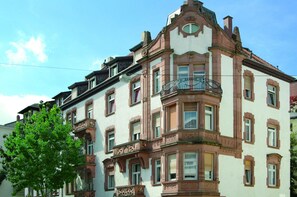 Un edificio de varios pisos con detalles arquitectónicos ornamentales, incluyendo un balcón con barandilla de hierro forjado.