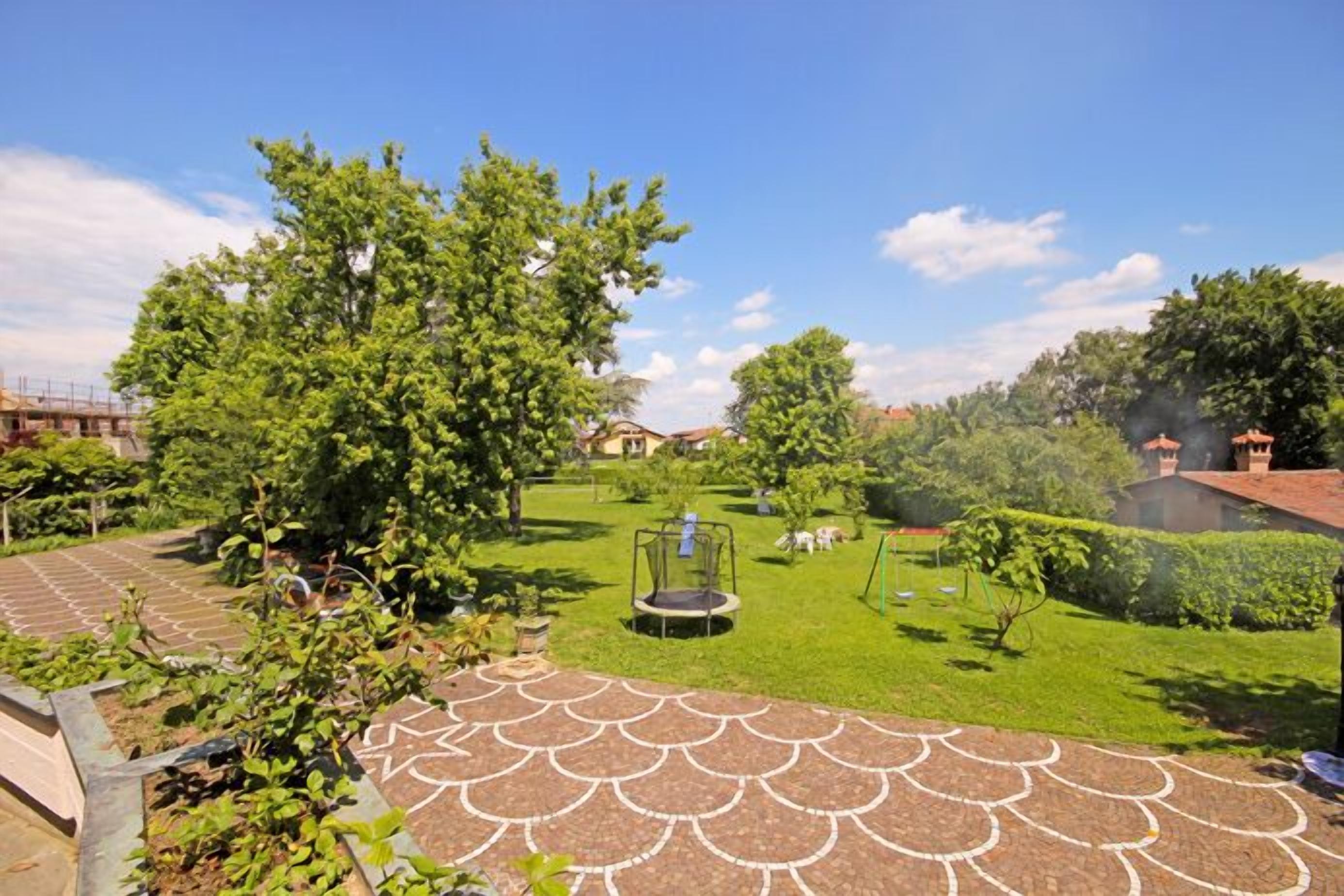 A garden with a trampoline, a swing set, and a paved area with a decorative pattern.