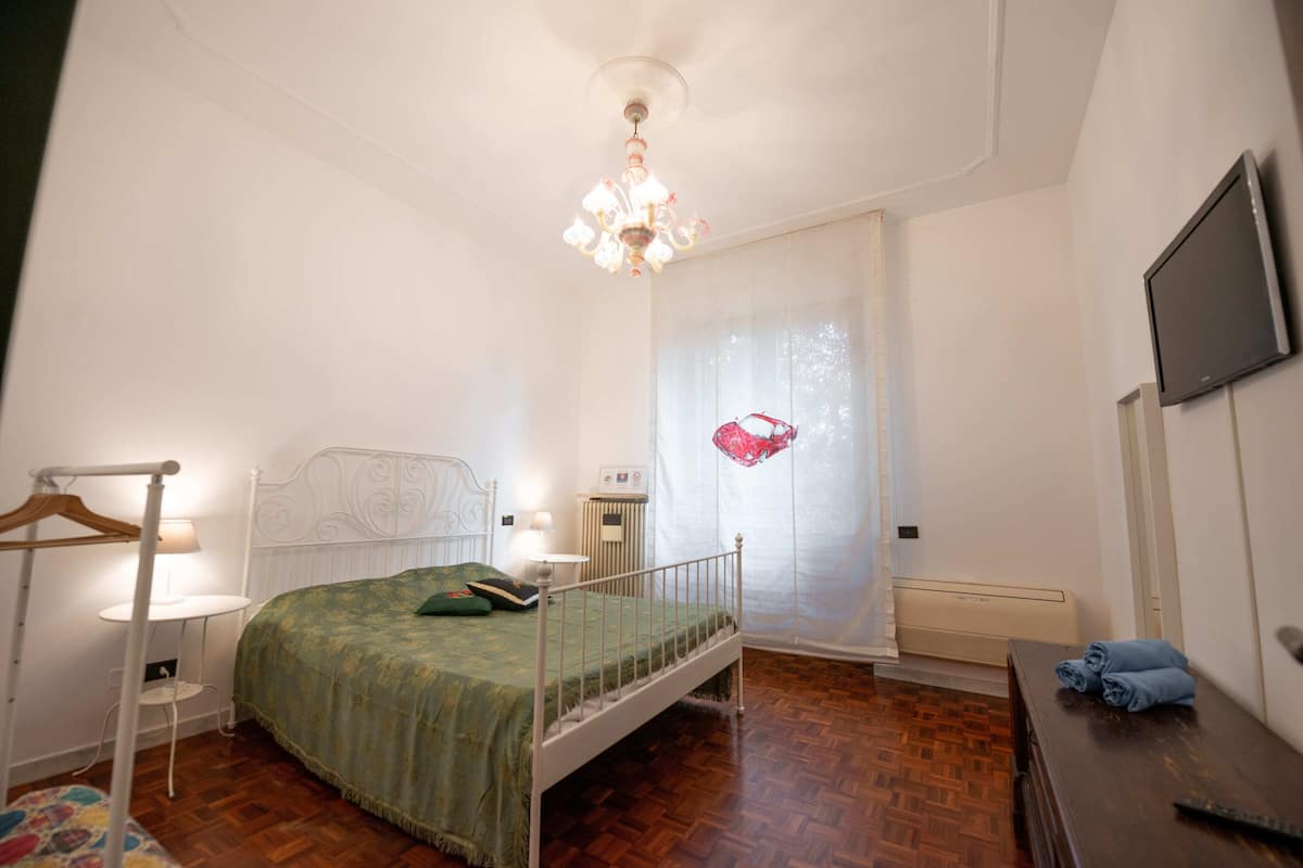A bedroom with a bed, bedside table, lamp, and a television on the wall.