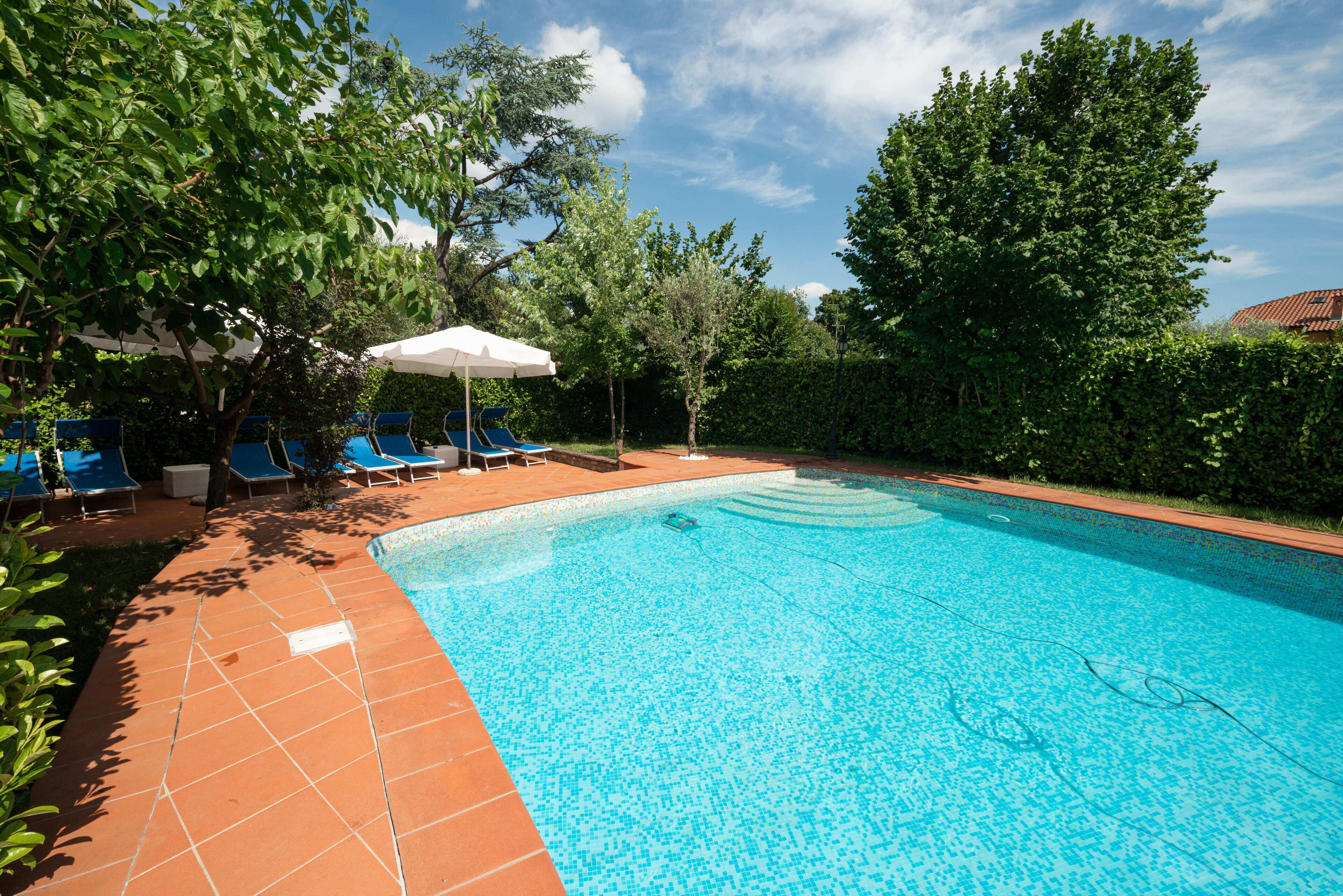 A swimming pool with blue tiles, surrounded by green trees and blue lounge chairs.