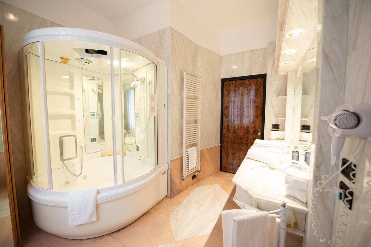 A modern bathroom with a glass-enclosed shower, a white bathtub, and a built-in hairdryer.