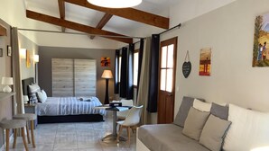 A modern hotel room with a bed, a sofa, a desk, and a chair. There is a window with curtains, a lamp, and artwork on the walls. - Chambres d'hôtes Rêv'de Thau (Balaruc-les-Bains)