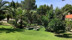 A lush garden with palm trees, a lawn, and a building with a red roof. - Chambres d'hôtes Rêv'de Thau (Balaruc-les-Bains)