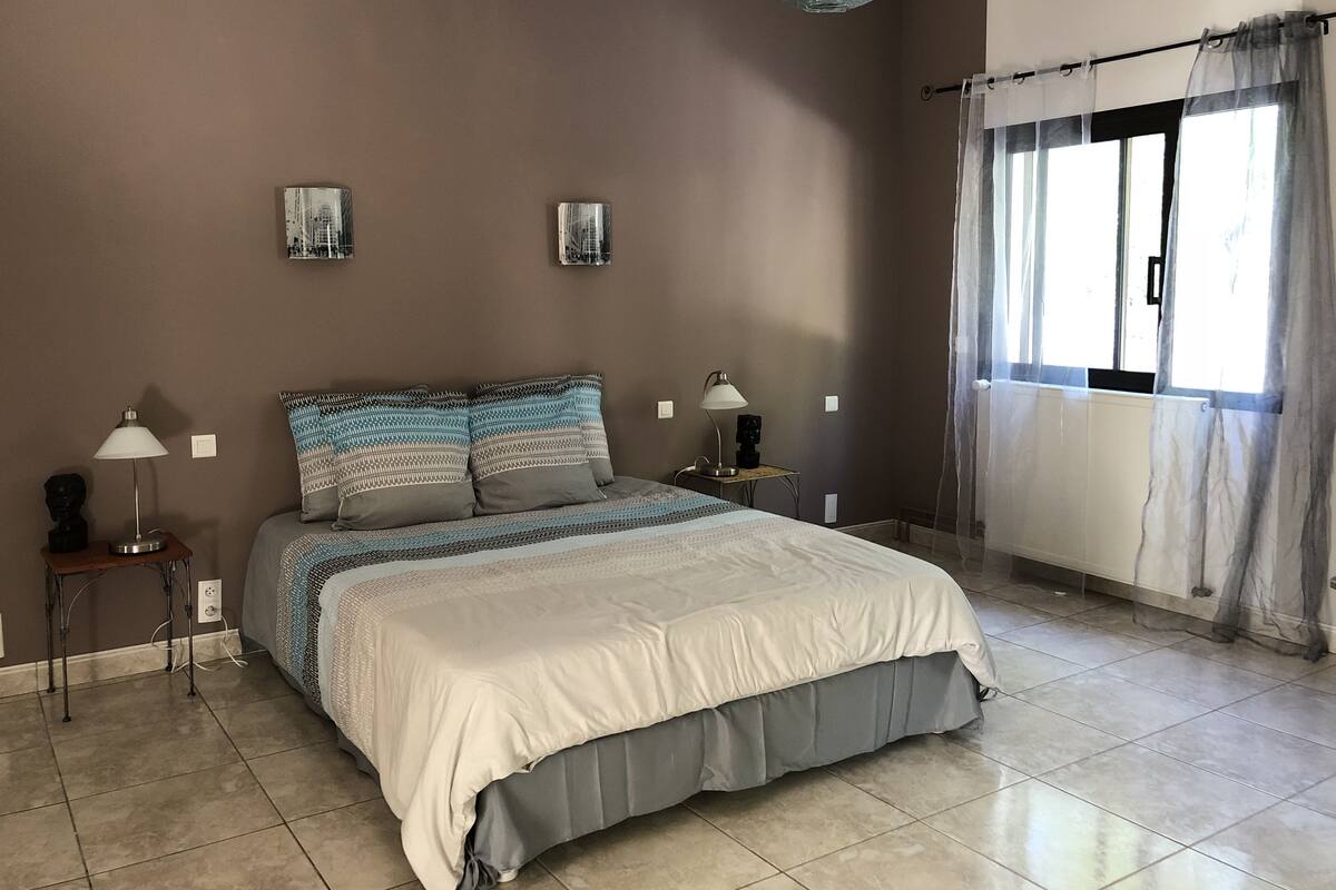 A bedroom with a bed, two bedside tables, a window with curtains, and a wall-mounted light fixture.