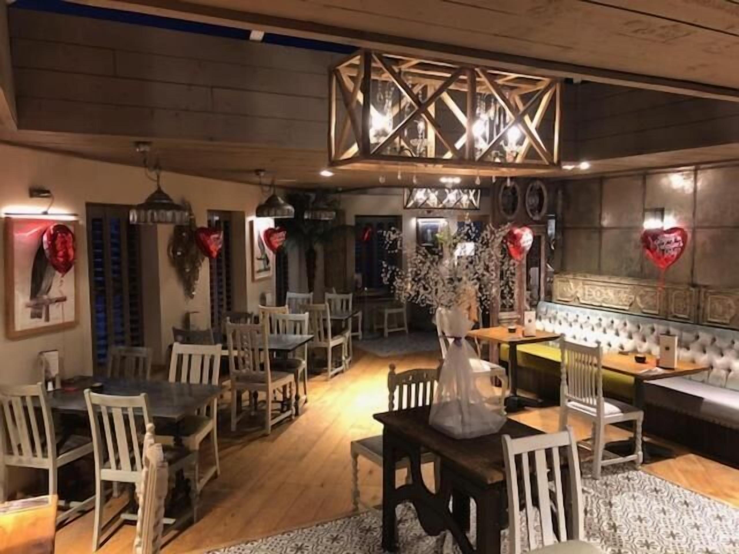Un restaurante con mesas y sillas de madera, una zona de estar central y decoraciones con forma de corazón en las paredes.