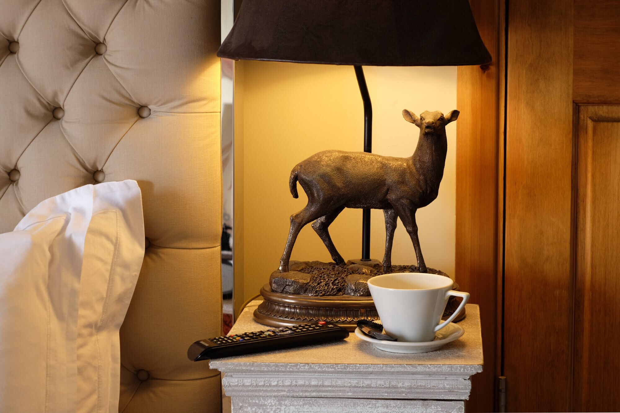 Ein Nachttisch mit Lampe, Fernbedienung, Tasse und einer Hirschfigur.
