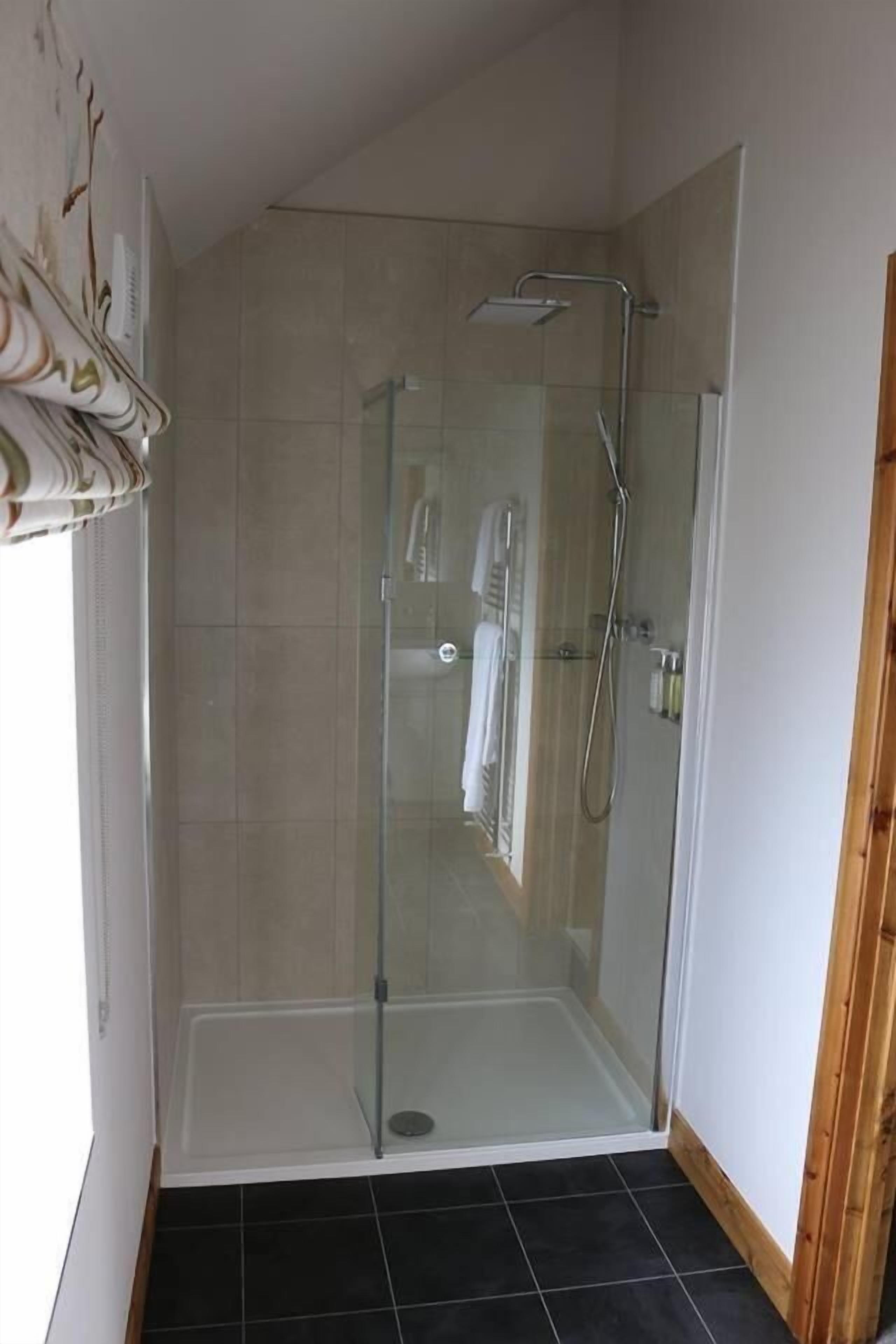 A glass-enclosed shower stall with a white tiled floor and a towel rack inside.