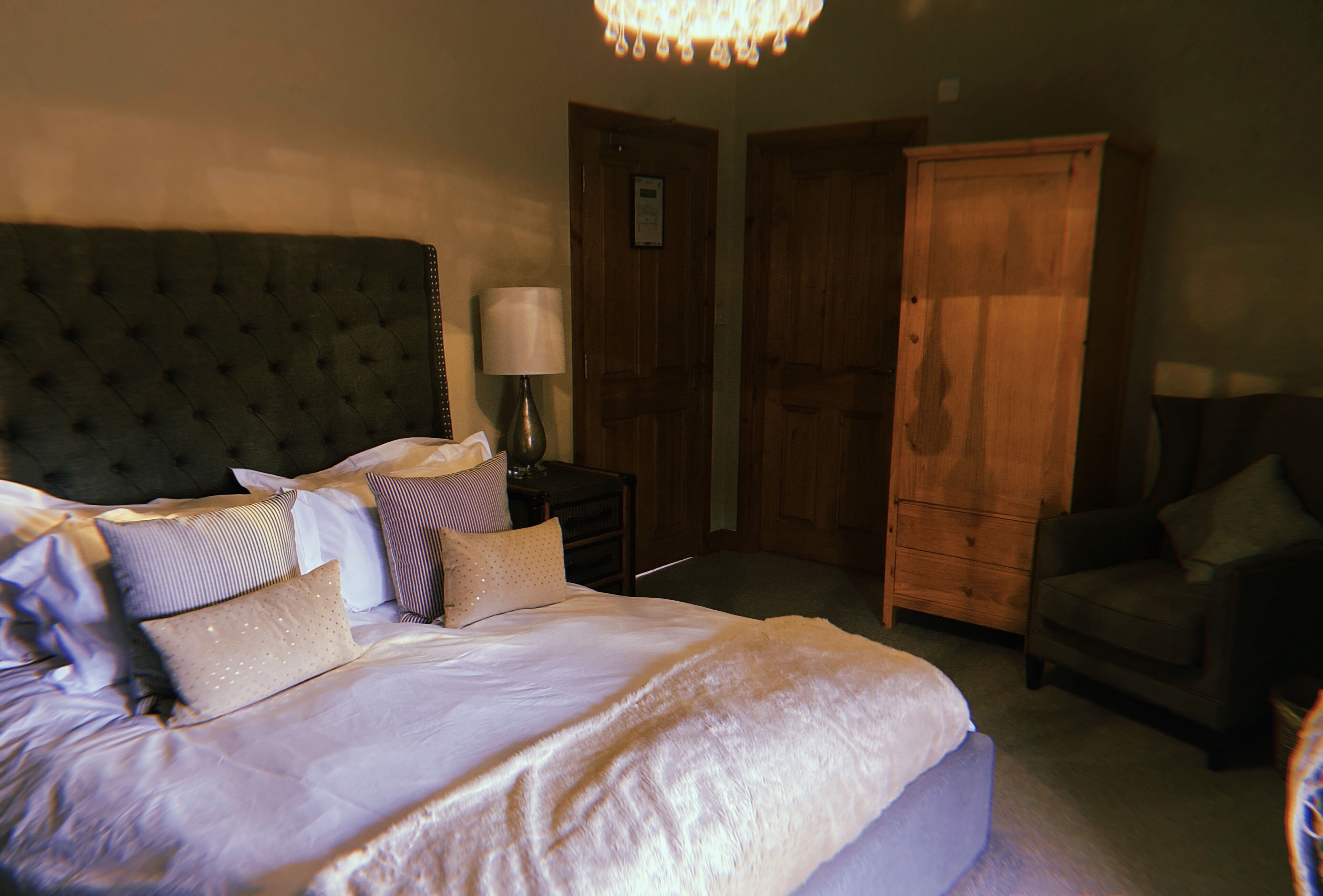 A bedroom with a large bed, a wooden wardrobe, a nightstand, and a chair.