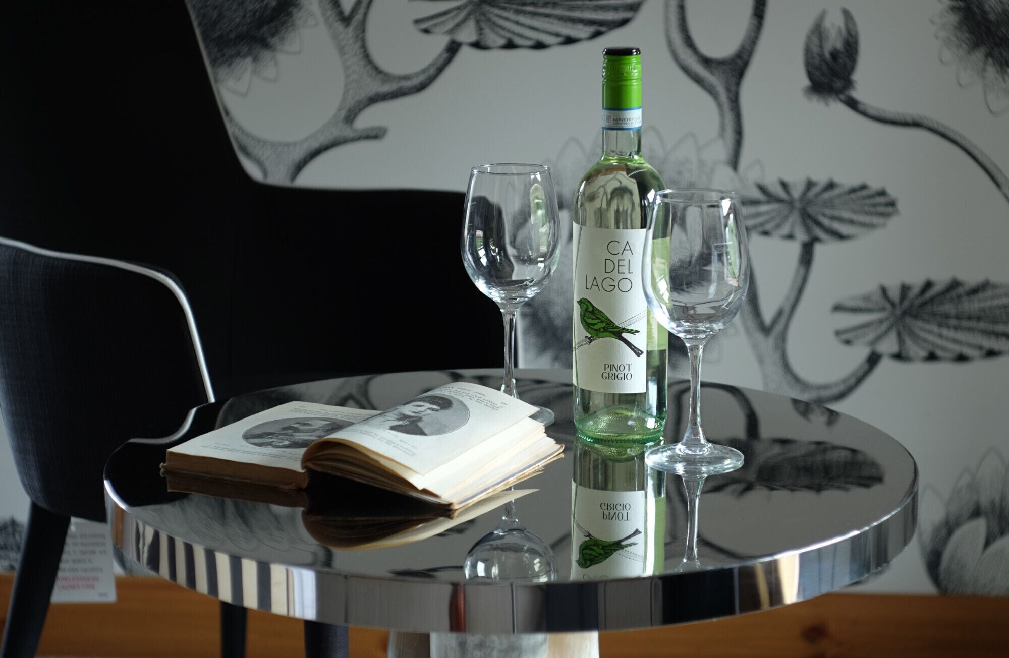 A table with a bottle of wine, two glasses, and a book.