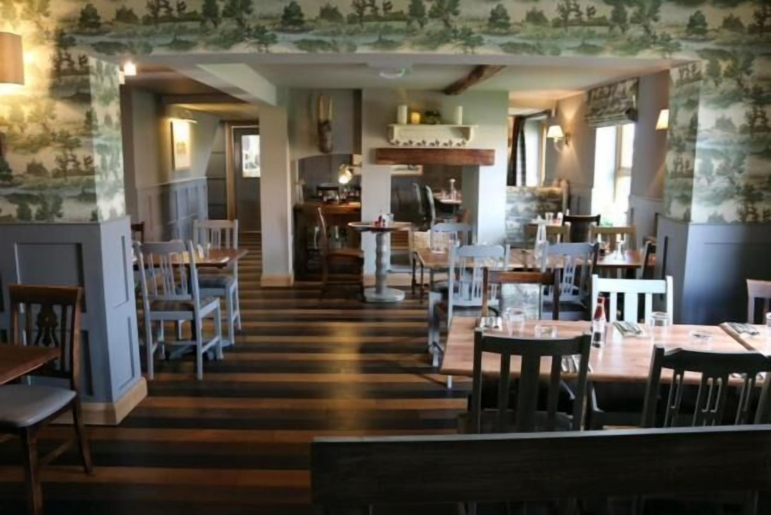 Un ristorante con pavimento in legno, sedie e tavoli bianchi. Si nota una scala che conduce a un'altra zona.