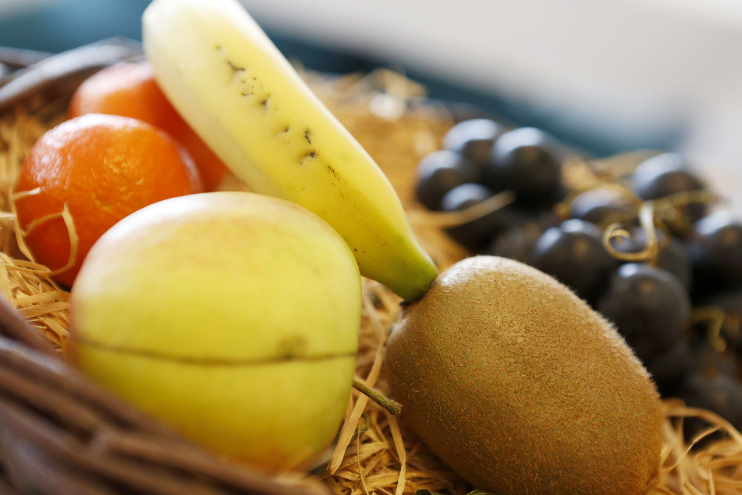 A basket containing various fruits including a banana, an orange, a kiwi, and grapes.