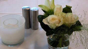 Una mesa dispuesta con una vela en vidrio transparente, un florero de vidrio con flores blancas y dos saleros y pimenteros.