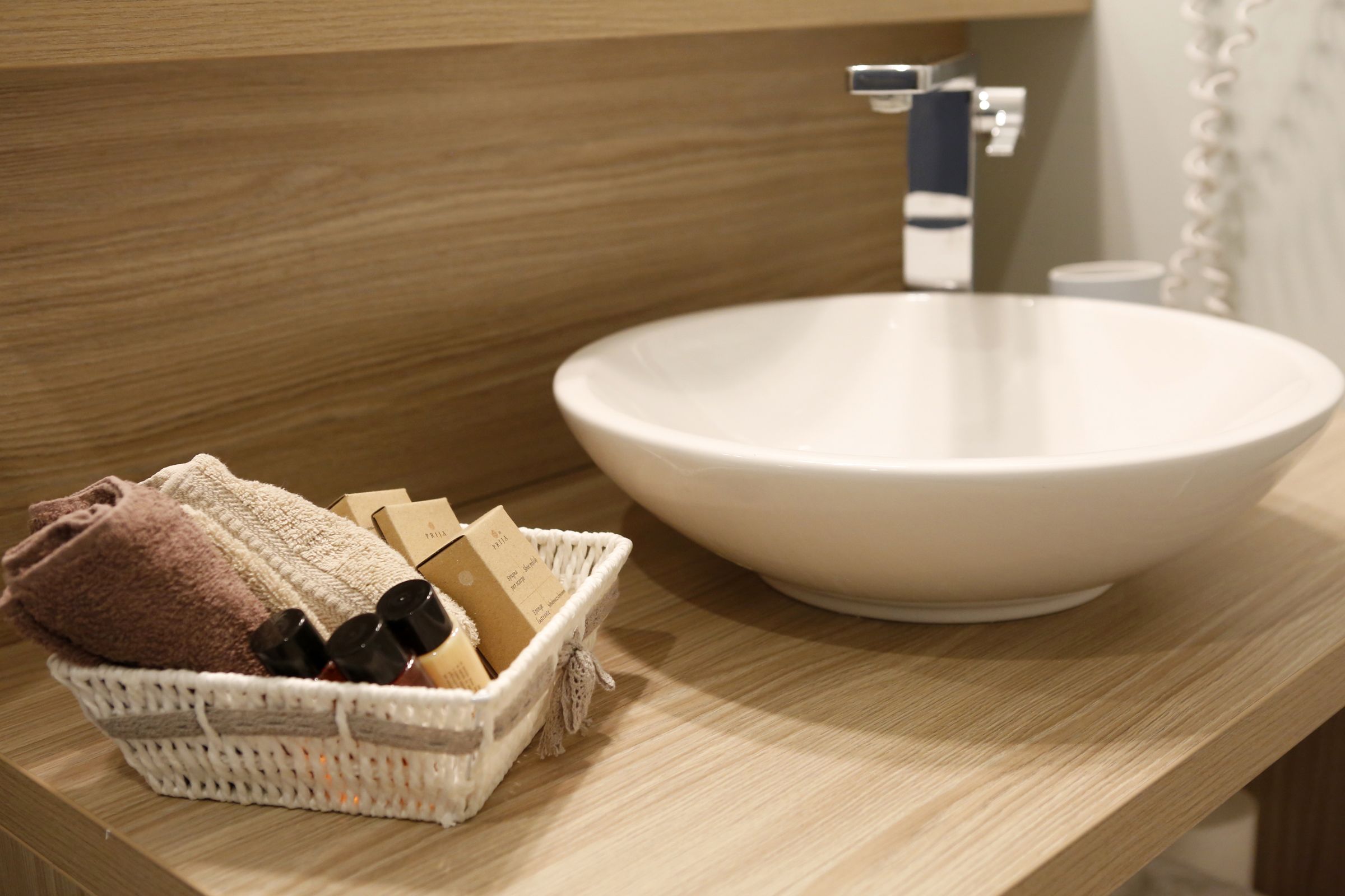 Un baño con un lavamanos de cerámica blanca, encimera de madera y una cesta de mimbre con toallas y artículos de aseo.