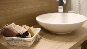 Un baño con un lavamanos de cerámica blanca, encimera de madera y una cesta de mimbre con toallas y artículos de aseo.